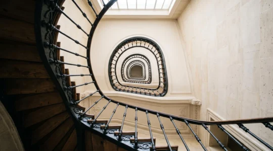 Escalier en colimaçon d'un immeuble haussmannien vu en contre-plongée, symbolisant l'ascension structurée des positions Google